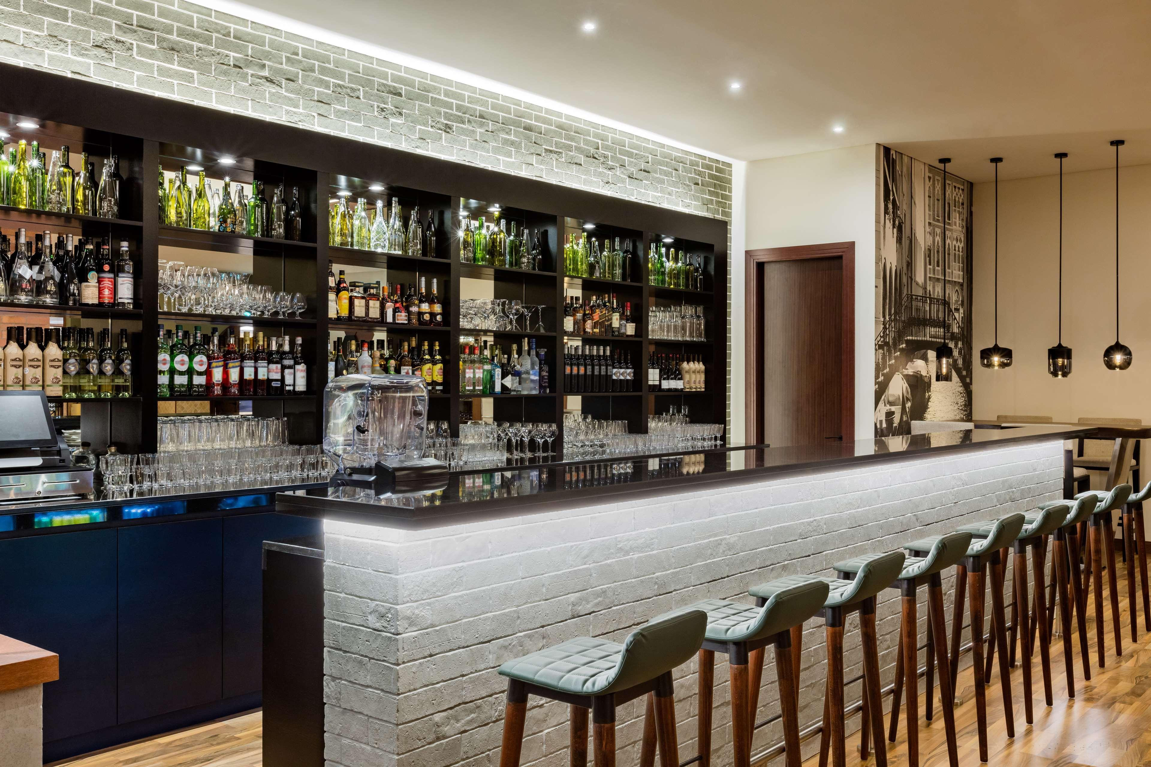 The Diplomat Radisson Blu Hotel Residence & Spa Manama Exterior photo The image shows a modern bar setup. The bar features a sleek, long counter made of dark material with integrated lighting that creates a soft glow. Behind the bar, there are shelves filled with a variety of bottles, including spirits and liquors, alo